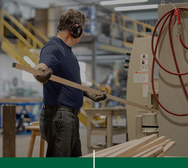 Un assistant opérateur, membre de l'équipe de Moulures 4D, qui utilise une des machines de transformation du bois de l'atelier.