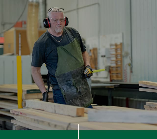 Un opérateur de scie, membre de l'équipe de Moulures 4D, qui mesure des planches de bois franc dans l'atelier de travail.